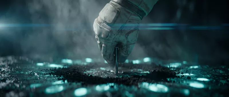 A gloved hand pushes a small metal beacon into dark ground scattered with turquoise lights.